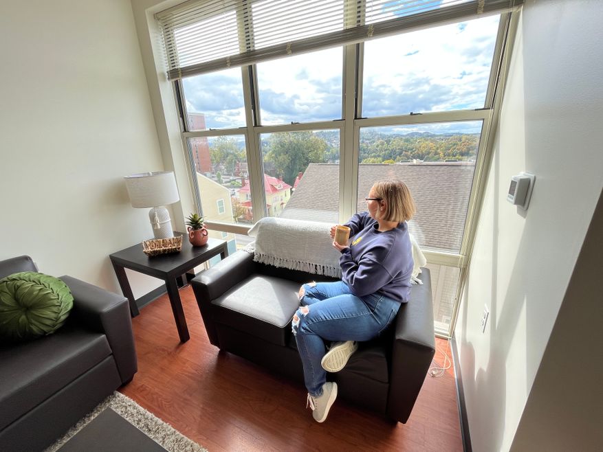 Student sitting on couch in University Place apartments looking out the window holding a coffee cup.
